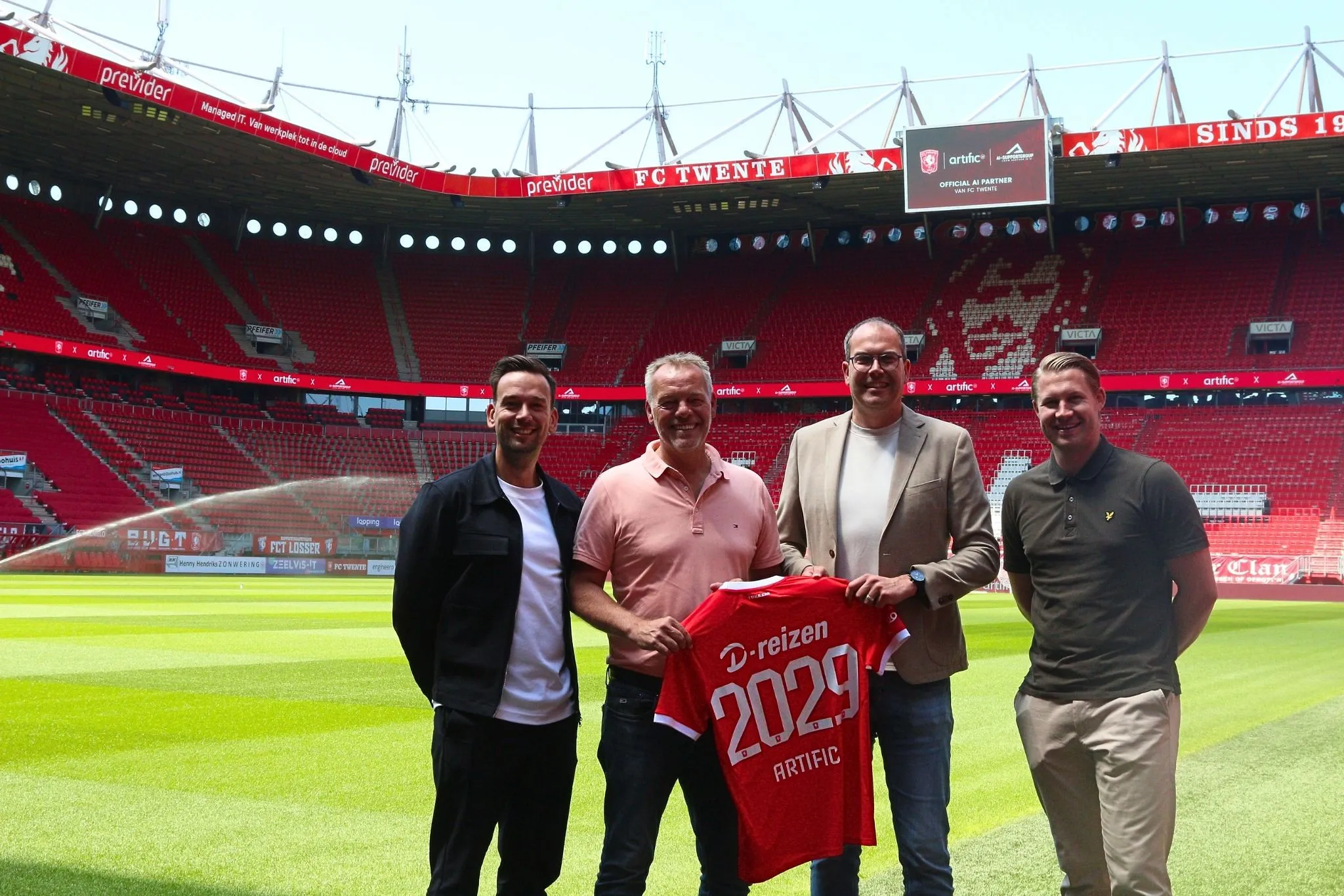 Four men on the pitch of De Grolsch Veste holding a red FC Twente shirt printed with 2029 and Artific, with Official AI Partner van FC Twente on the scoreboard.