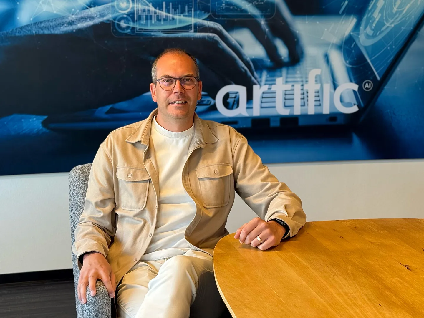 Ivo Rupert sitting at a wooden table in front of a wall poster with the Artific logo.