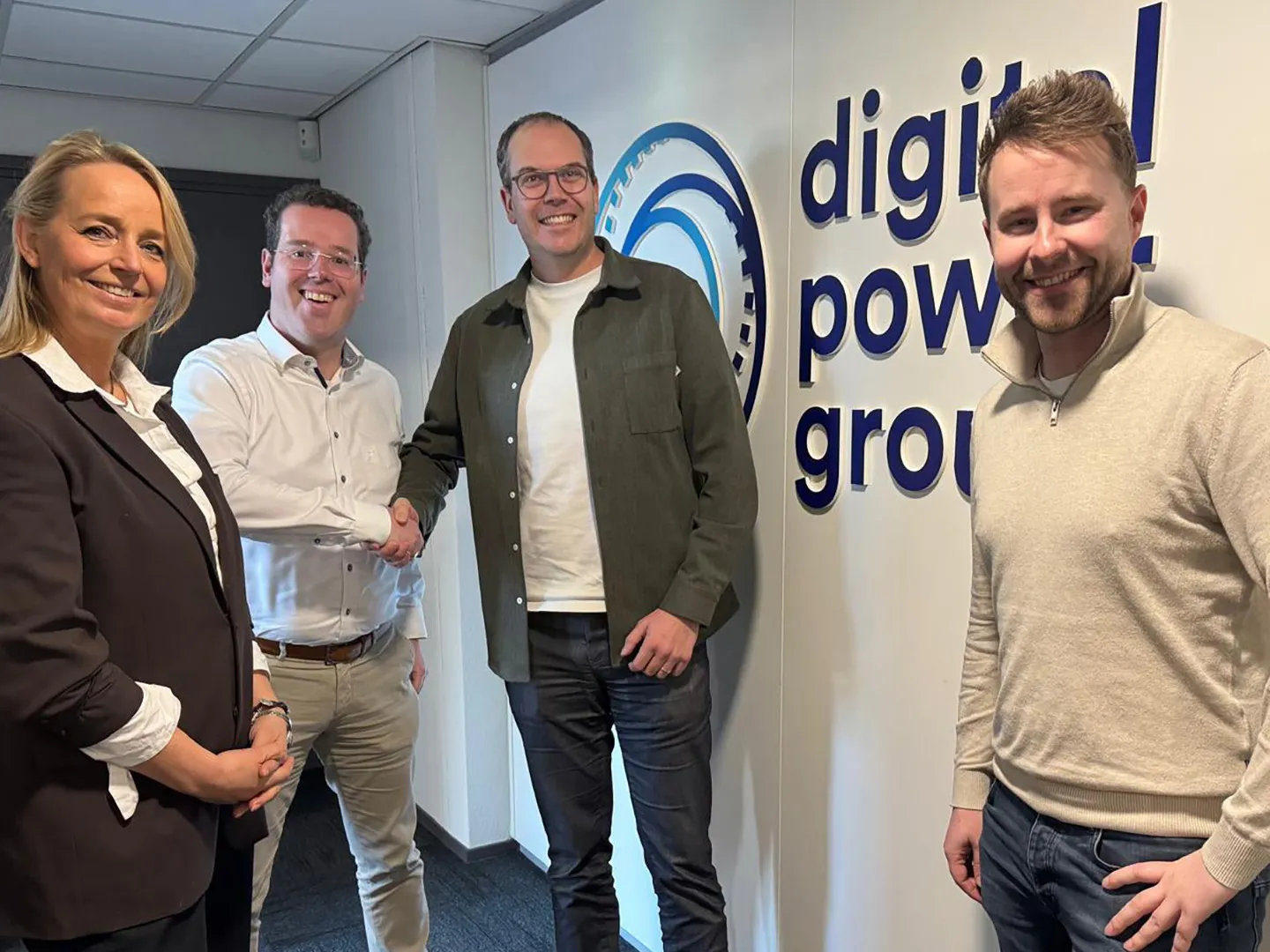 Four people by a wall with the Digital Power Group logo, two of them shaking hands.