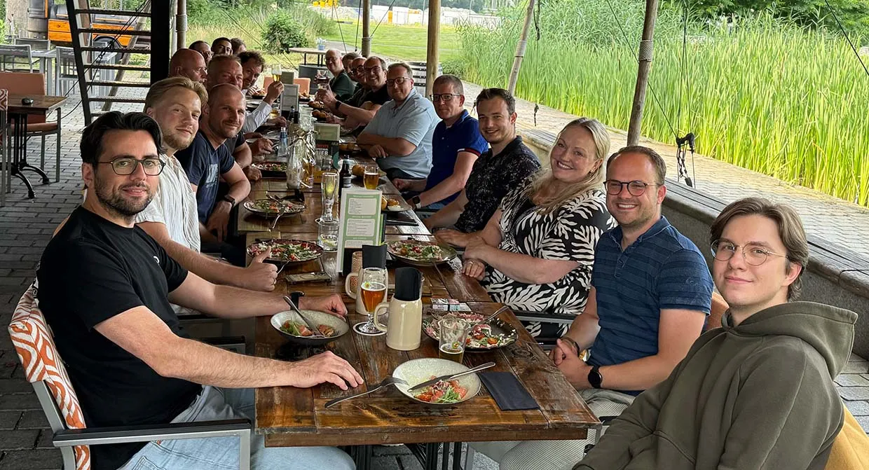 The Artific team at a long wooden table on a terrace, with plates and glasses in front of them, laughing at the camera.