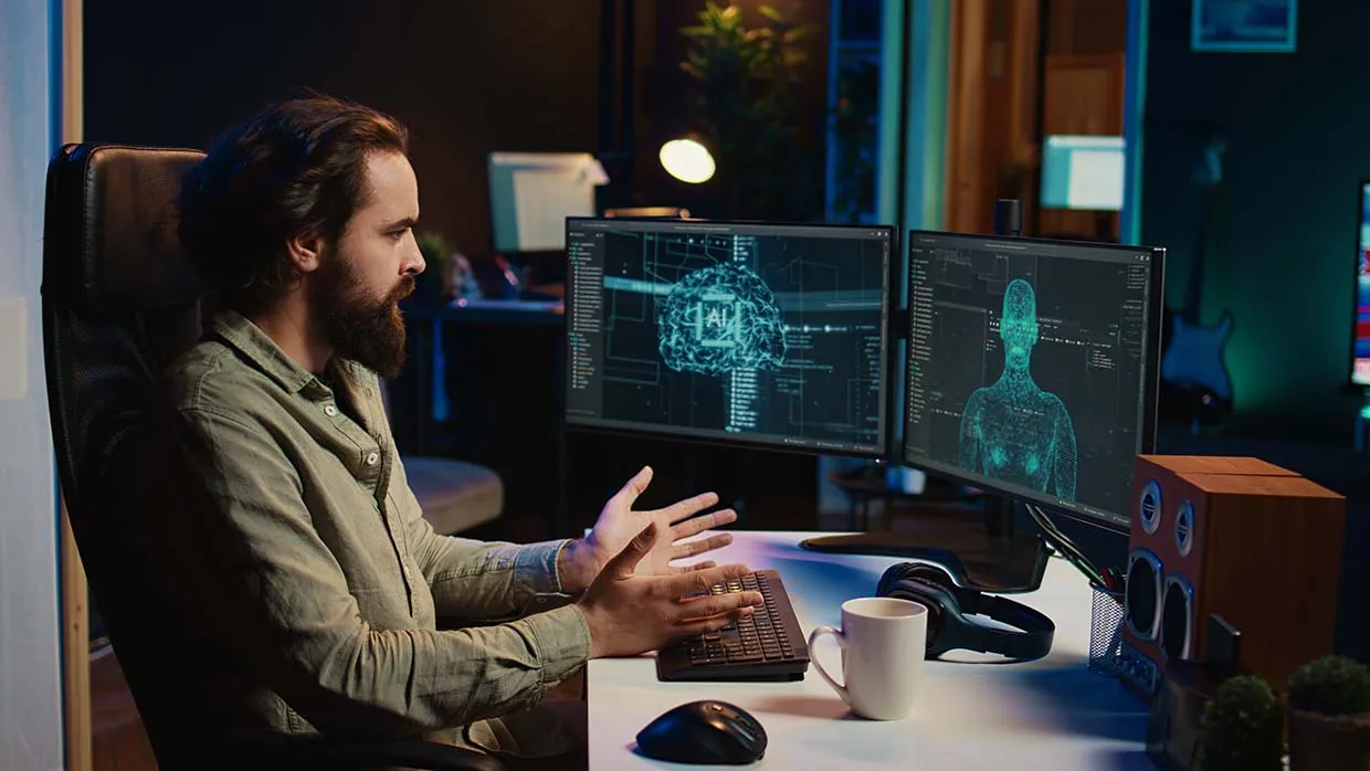 A bearded man behind two monitors, showing a glowing brain and a human figure made of blue dots.